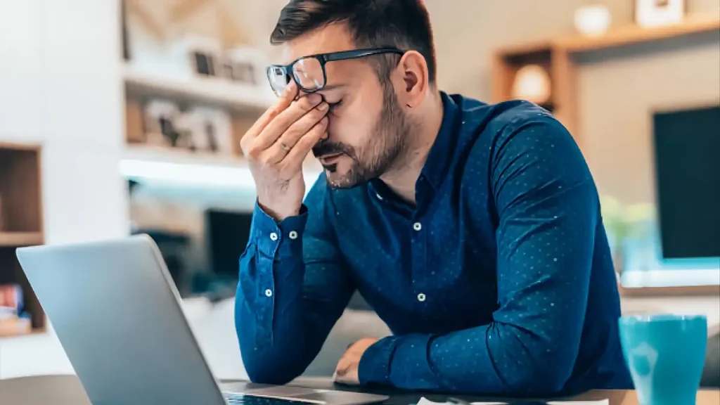 Homem cansado e frustrado olhando para o notebook após muito esforço sem entender por que nada muda na sua vida.